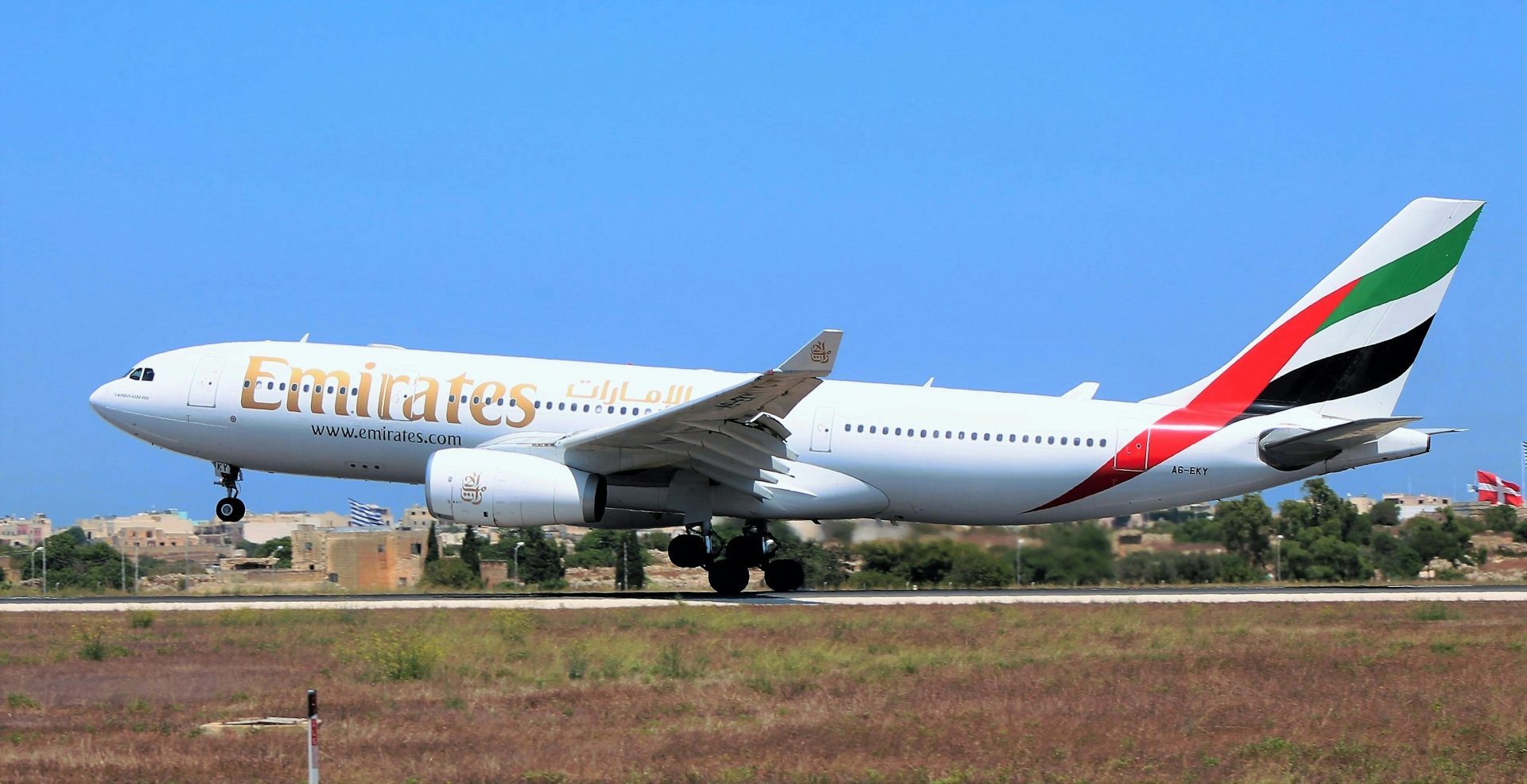 Wide-body Emirates aircraft taking off from Malta's airport on a clear day.